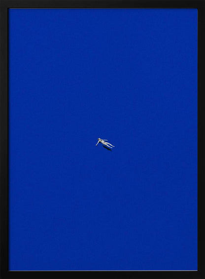 A minimalist and surreal artwork featuring a tiny, pale human figure floating peacefully in the center of an immense, solid, and vibrant blue void, all enclosed within a thin black frame. Wall Art