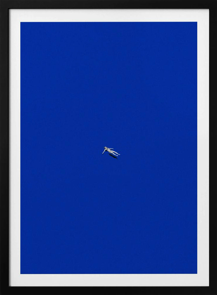 A minimalist and surreal artwork featuring a tiny, pale human figure floating peacefully in the center of an immense, solid, and vibrant blue void, all enclosed within a thin black frame. Wall Art