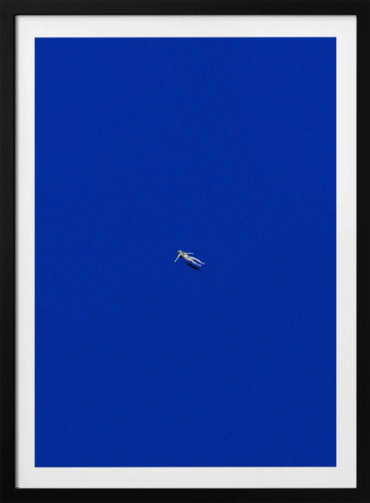 A minimalist and surreal artwork featuring a tiny, pale human figure floating peacefully in the center of an immense, solid, and vibrant blue void, all enclosed within a thin black frame. Wall Art