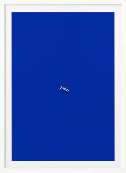 A minimalist and surreal artwork featuring a tiny, pale human figure floating peacefully in the center of an immense, solid, and vibrant blue void, all enclosed within a thin black frame. Wall Art