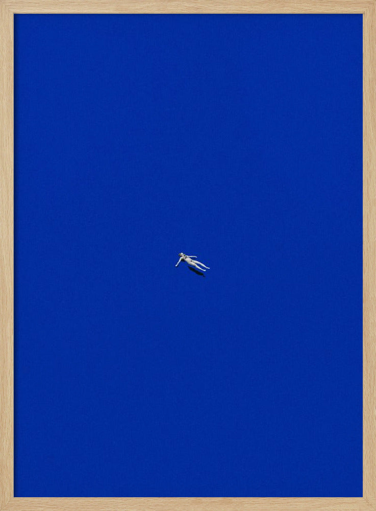 A minimalist and surreal artwork featuring a tiny, pale human figure floating peacefully in the center of an immense, solid, and vibrant blue void, all enclosed within a thin black frame. Wall Art