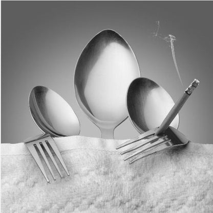 A conceptual black and white photograph in a light wood frame, featuring three spoons standing upright on a white towel, while a fork in the foreground holds a lit, smoking cigarette between its tines. Wall Art