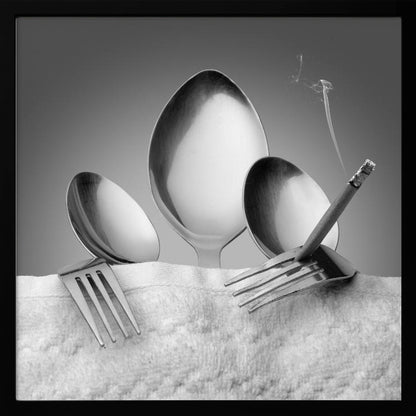 A conceptual black and white photograph in a light wood frame, featuring three spoons standing upright on a white towel, while a fork in the foreground holds a lit, smoking cigarette between its tines. Wall Art