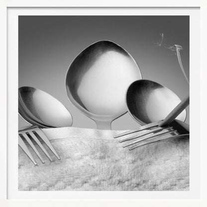 A conceptual black and white photograph in a light wood frame, featuring three spoons standing upright on a white towel, while a fork in the foreground holds a lit, smoking cigarette between its tines. Wall Art
