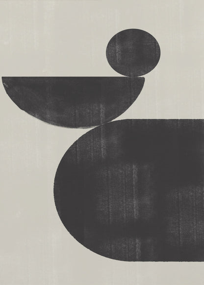 A minimalist abstract artwork featuring three charcoal black shapes stacked against a light beige textured background. At the bottom is a large, rounded shape, on which a semi-circle is balanced. A smaller, full circle rests on top of the semi-circle, creating a sense of precarious balance. The piece is enclosed in a simple black frame. Decor