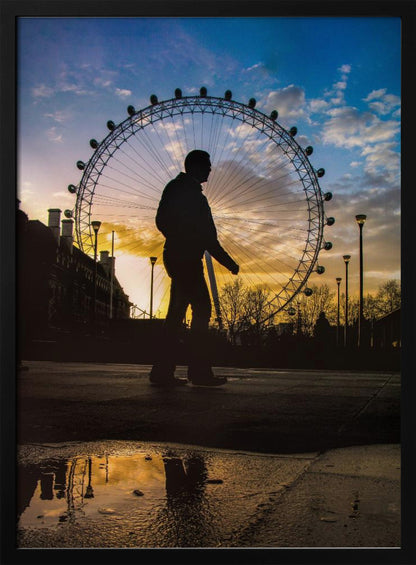 A low-angle shot of a person's silhouette walking past the London Eye at sunset, with the vibrant orange and blue sky reflected in a puddle in the foreground. Decor