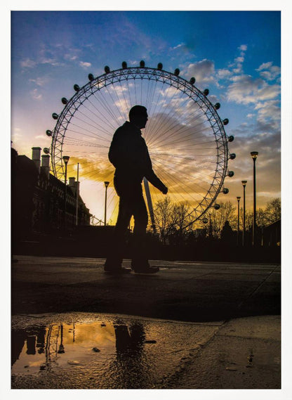 A low-angle shot of a person's silhouette walking past the London Eye at sunset, with the vibrant orange and blue sky reflected in a puddle in the foreground. Decor