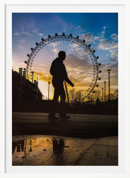 A low-angle shot of a person's silhouette walking past the London Eye at sunset, with the vibrant orange and blue sky reflected in a puddle in the foreground. Decor