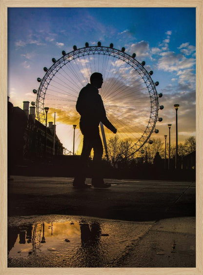 A low-angle shot of a person's silhouette walking past the London Eye at sunset, with the vibrant orange and blue sky reflected in a puddle in the foreground. Decor