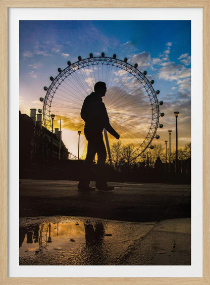 A low-angle shot of a person's silhouette walking past the London Eye at sunset, with the vibrant orange and blue sky reflected in a puddle in the foreground. Decor