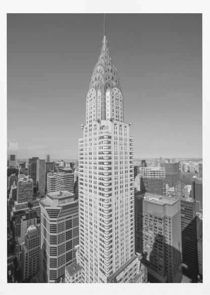A high-angle, black and white photograph of the iconic Chrysler Building, its Art Deco spire prominently featured against the New York City skyline under a clear sky. Artwork