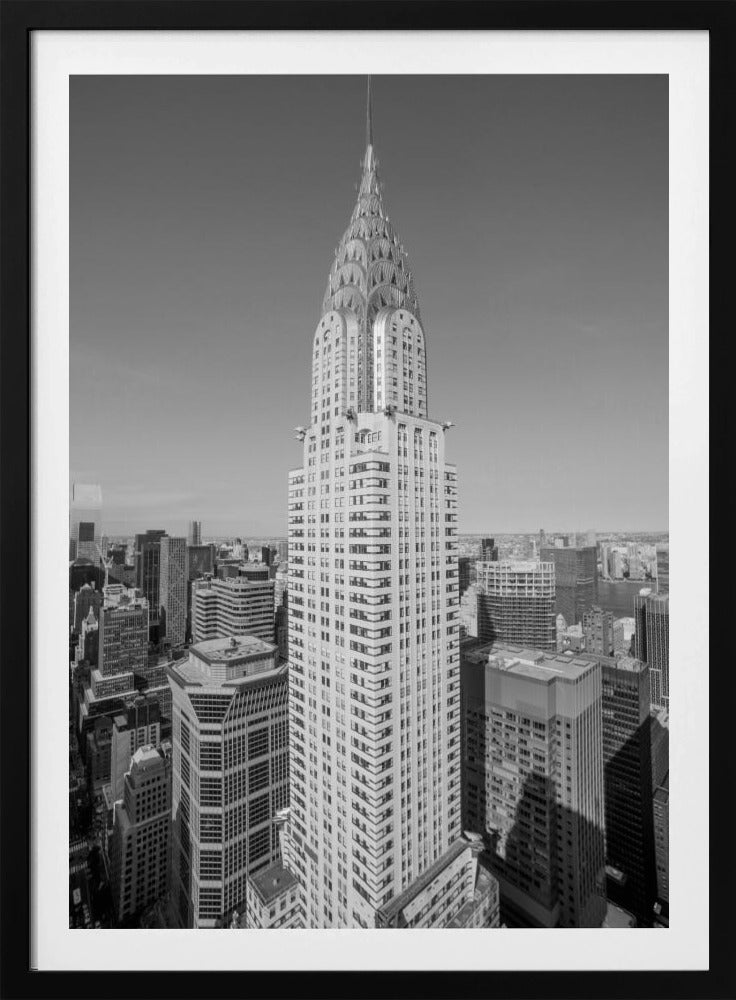 A high-angle, black and white photograph of the iconic Chrysler Building, its Art Deco spire prominently featured against the New York City skyline under a clear sky. Artwork