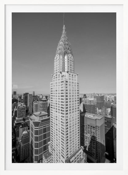 A high-angle, black and white photograph of the iconic Chrysler Building, its Art Deco spire prominently featured against the New York City skyline under a clear sky. Artwork