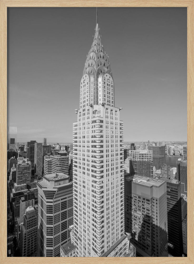 A high-angle, black and white photograph of the iconic Chrysler Building, its Art Deco spire prominently featured against the New York City skyline under a clear sky. Artwork