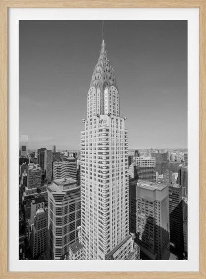 A high-angle, black and white photograph of the iconic Chrysler Building, its Art Deco spire prominently featured against the New York City skyline under a clear sky. Artwork