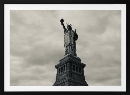 A low-angle, black and white photograph of the Statue of Liberty standing tall against a cloudy, dramatic sky, enclosed in a silver frame. Poster