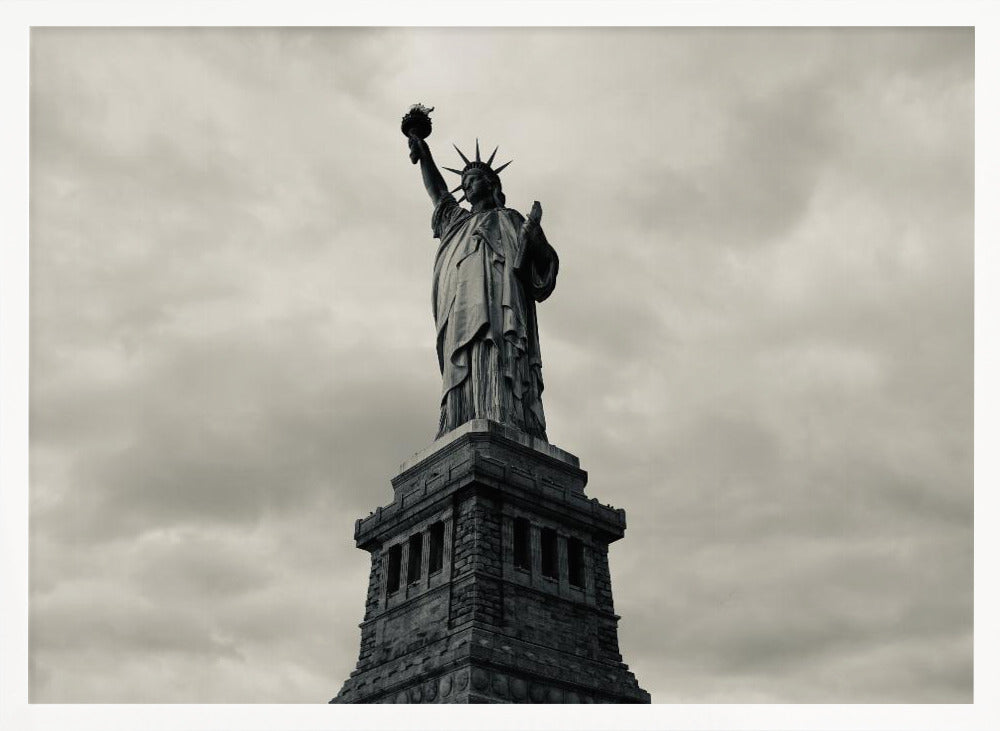 A low-angle, black and white photograph of the Statue of Liberty standing tall against a cloudy, dramatic sky, enclosed in a silver frame. Poster