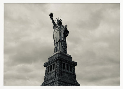 A low-angle, black and white photograph of the Statue of Liberty standing tall against a cloudy, dramatic sky, enclosed in a silver frame. Poster