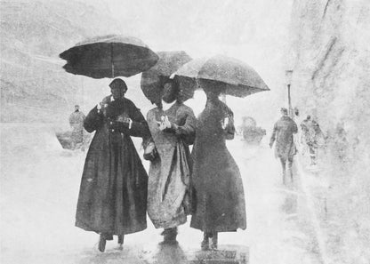 A vintage black and white photograph in a silver frame, depicting three people in long dark coats walking together under umbrellas during a heavy snow or rain storm on a city street. The image has a grainy, textured quality, giving it an old-fashioned, artistic feel. Poster