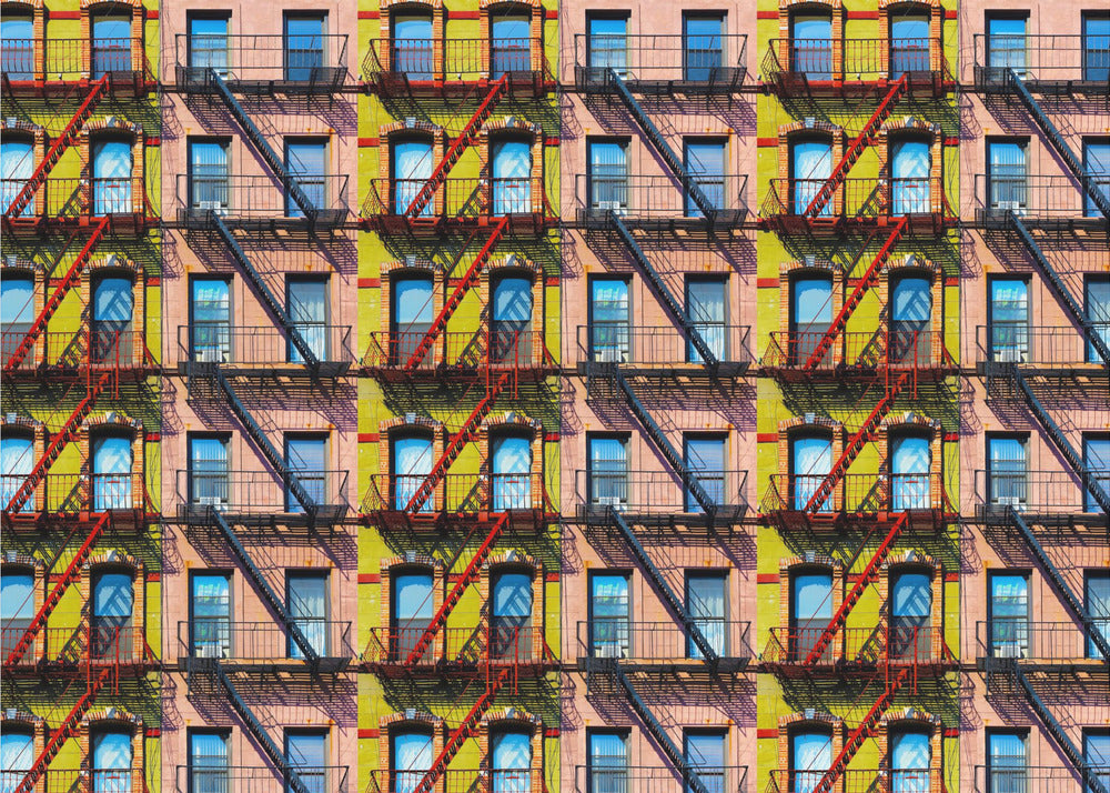 A pop-art style repeating pattern of a colorful apartment building facade featuring pink and yellow walls, windows reflecting a blue sky, and a network of black and red fire escapes, enclosed in a silver frame. Artwork