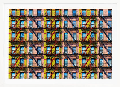 A pop-art style repeating pattern of a colorful apartment building facade featuring pink and yellow walls, windows reflecting a blue sky, and a network of black and red fire escapes, enclosed in a silver frame. Artwork