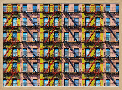 A pop-art style repeating pattern of a colorful apartment building facade featuring pink and yellow walls, windows reflecting a blue sky, and a network of black and red fire escapes, enclosed in a silver frame. Artwork
