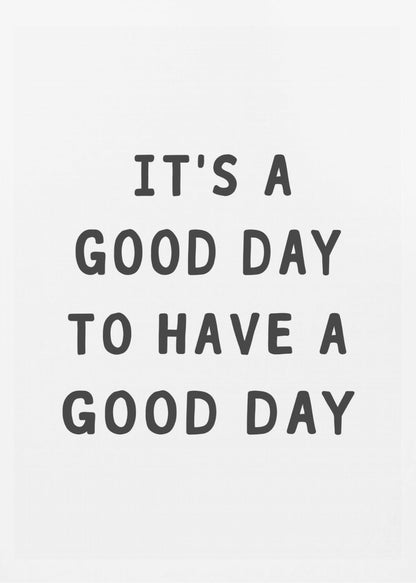 A framed black and white art print with the phrase 'IT'S A GOOD DAY TO HAVE A GOOD DAY' in a bold, dark gray, sans-serif font. Artwork