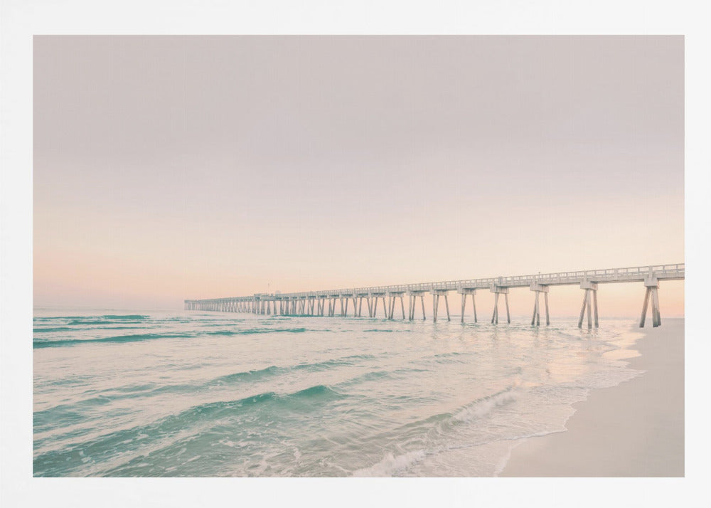 A tranquil beach scene with a long white pier extending into the turquoise ocean. The sky is a soft, pale pink, suggesting a serene sunrise or sunset, and gentle waves lap onto the sandy shore in the foreground. Poster