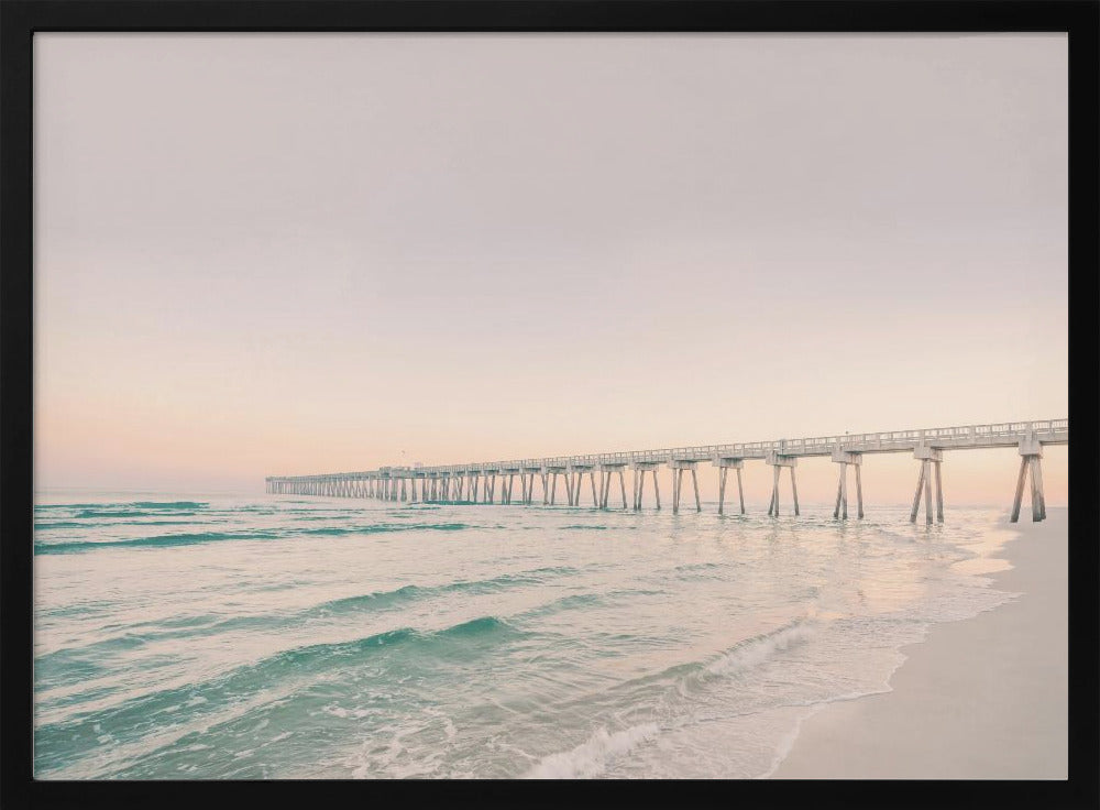 A tranquil beach scene with a long white pier extending into the turquoise ocean. The sky is a soft, pale pink, suggesting a serene sunrise or sunset, and gentle waves lap onto the sandy shore in the foreground. Poster