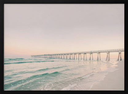 A tranquil beach scene with a long white pier extending into the turquoise ocean. The sky is a soft, pale pink, suggesting a serene sunrise or sunset, and gentle waves lap onto the sandy shore in the foreground. Poster