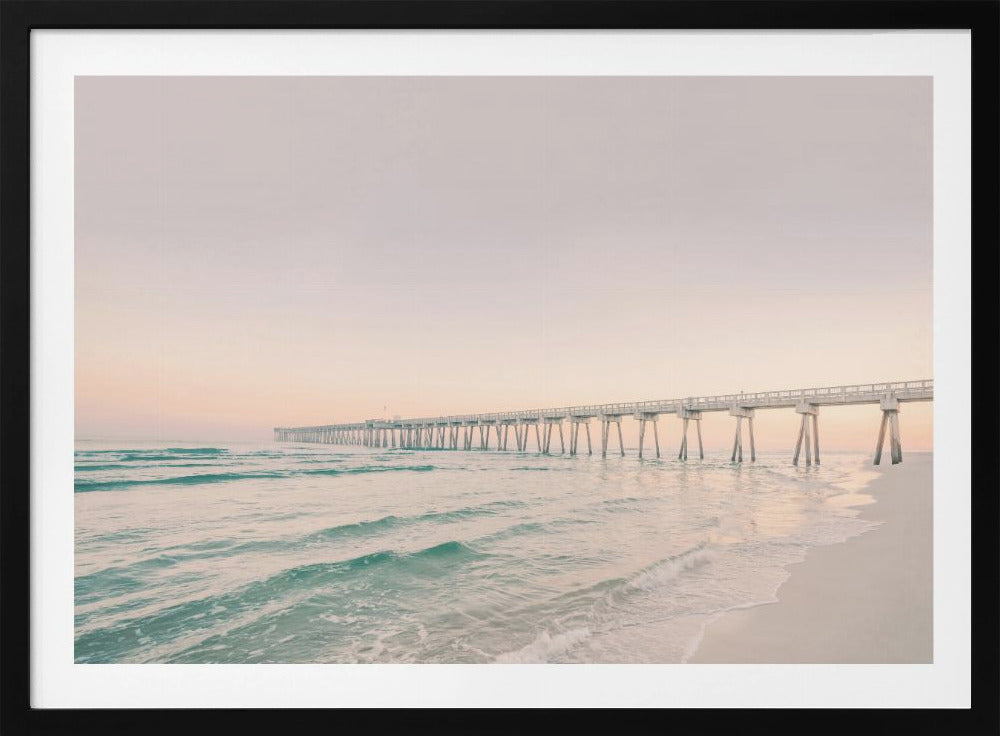A tranquil beach scene with a long white pier extending into the turquoise ocean. The sky is a soft, pale pink, suggesting a serene sunrise or sunset, and gentle waves lap onto the sandy shore in the foreground. Poster