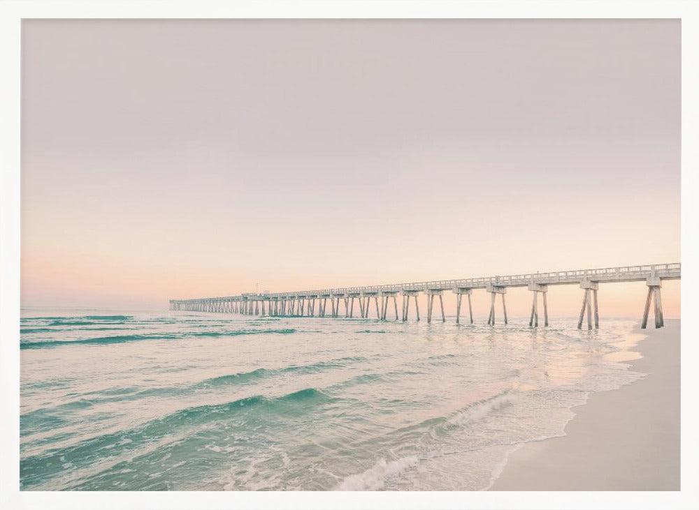 A tranquil beach scene with a long white pier extending into the turquoise ocean. The sky is a soft, pale pink, suggesting a serene sunrise or sunset, and gentle waves lap onto the sandy shore in the foreground. Poster