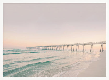 A tranquil beach scene with a long white pier extending into the turquoise ocean. The sky is a soft, pale pink, suggesting a serene sunrise or sunset, and gentle waves lap onto the sandy shore in the foreground. Poster
