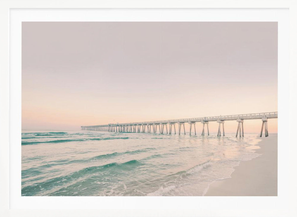 A tranquil beach scene with a long white pier extending into the turquoise ocean. The sky is a soft, pale pink, suggesting a serene sunrise or sunset, and gentle waves lap onto the sandy shore in the foreground. Poster