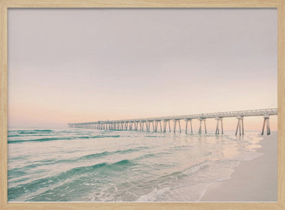 A tranquil beach scene with a long white pier extending into the turquoise ocean. The sky is a soft, pale pink, suggesting a serene sunrise or sunset, and gentle waves lap onto the sandy shore in the foreground. Poster