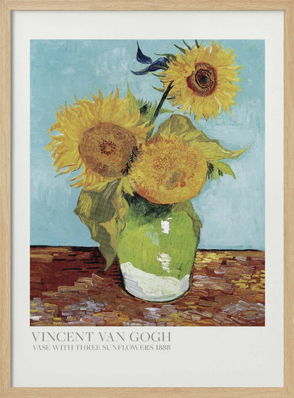 A framed art print of Vincent van Gogh's painting 'Vase with Three Sunflowers' from 1888. The artwork features three large, vibrant yellow sunflowers in a green vase set against a textured light blue background. The painting is in the post-impressionist style with thick, visible brushstrokes. The print has a white border with text at the bottom identifying the artist and title. Print