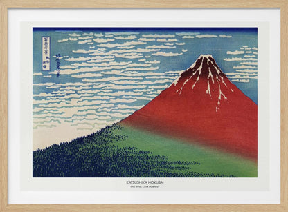 A framed Japanese woodblock print, 'Fine Wind, Clear Morning' by Katsushika Hokusai, also known as 'Red Fuji'. The print depicts a large, reddish-brown Mount Fuji with its peak lightly dusted with snow, set against a vibrant blue sky filled with white, streaky clouds. A dark green forest covers the base of the mountain. Poster
