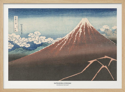 A framed Japanese woodblock print by Katsushika Hokusai titled 'Shower Below the Summit.' The print depicts a large, dark brown and reddish mountain, likely Mount Fuji, with a snow-capped peak. The sky above is a deep blue, and stylized white clouds are scattered around the mountain's slope. In the dark foreground, a jagged pink line represents a lightning strike. Artwork