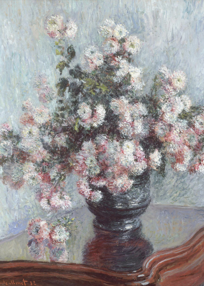 An impressionist painting by Claude Monet depicting a large bouquet of white and pink chrysanthemums in a dark, ornate vase. The vase sits on a reflective, reddish-brown wooden table, and the background is a textured light blue wall. The painting is framed in black. Artwork