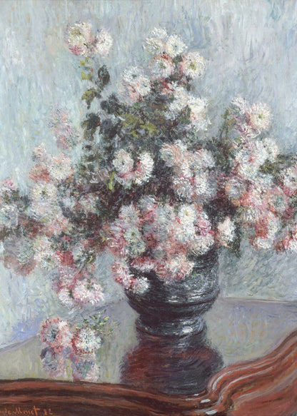 An impressionist painting by Claude Monet depicting a large bouquet of white and pink chrysanthemums in a dark, ornate vase. The vase sits on a reflective, reddish-brown wooden table, and the background is a textured light blue wall. The painting is framed in black. Artwork