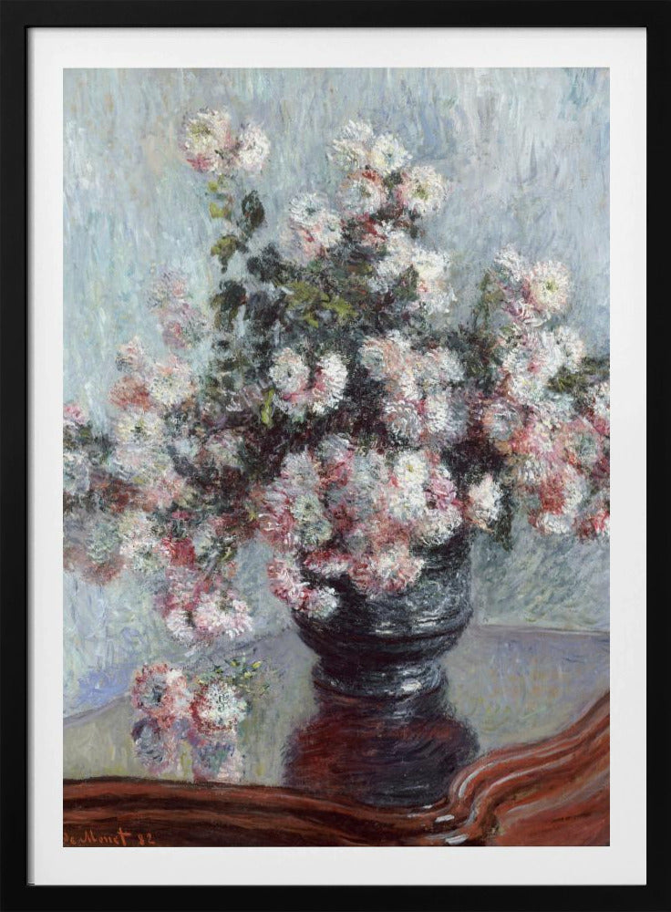 An impressionist painting by Claude Monet depicting a large bouquet of white and pink chrysanthemums in a dark, ornate vase. The vase sits on a reflective, reddish-brown wooden table, and the background is a textured light blue wall. The painting is framed in black. Artwork