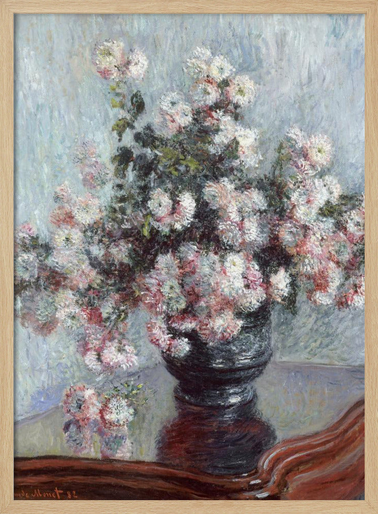 An impressionist painting by Claude Monet depicting a large bouquet of white and pink chrysanthemums in a dark, ornate vase. The vase sits on a reflective, reddish-brown wooden table, and the background is a textured light blue wall. The painting is framed in black. Artwork