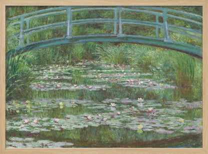 An Impressionist painting by Claude Monet depicting a green Japanese-style footbridge arching over a tranquil pond filled with blooming water lilies and lily pads, all rendered in soft, dappled brushstrokes and framed in a modern silver frame. Print