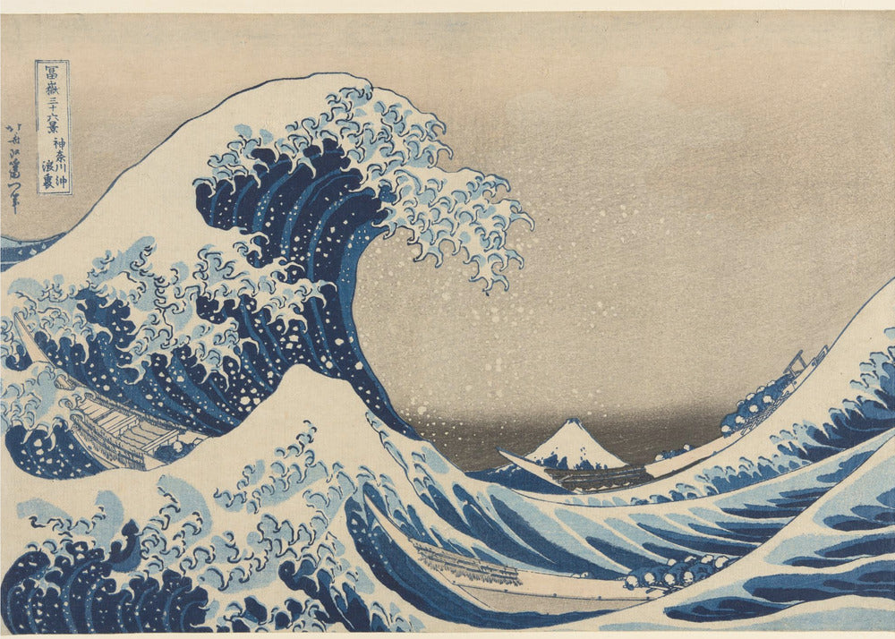 The Great Wave off Kanagawa by Hokusai, a famous Japanese ukiyo-e woodblock print. It depicts a massive, deep blue wave with claw-like white foam cresting and about to crash over three boats, with a small, snow-capped Mount Fuji visible in the background under a pale, graded sky. Artwork