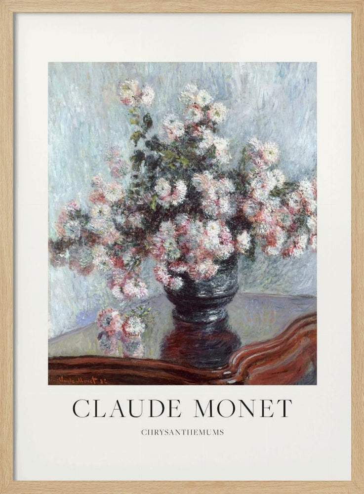 A framed art print of Claude Monet's impressionist painting, 'Chrysanthemums.' The painting features a lush bouquet of pink and white chrysanthemums in a dark vase resting on a reflective, mahogany-colored table against a light blue, textured background. The print includes a white border with the artist's name and the title below the artwork, all enclosed in a simple black frame. Print