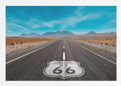 A framed photograph of the iconic Historic US Route 66 shield painted on a long, straight asphalt road that stretches through a desert landscape toward distant snow-capped mountains under a vibrant blue sky. Wall Art