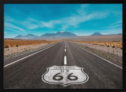 A framed photograph of the iconic Historic US Route 66 shield painted on a long, straight asphalt road that stretches through a desert landscape toward distant snow-capped mountains under a vibrant blue sky. Wall Art