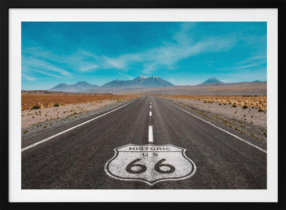 A framed photograph of the iconic Historic US Route 66 shield painted on a long, straight asphalt road that stretches through a desert landscape toward distant snow-capped mountains under a vibrant blue sky. Wall Art