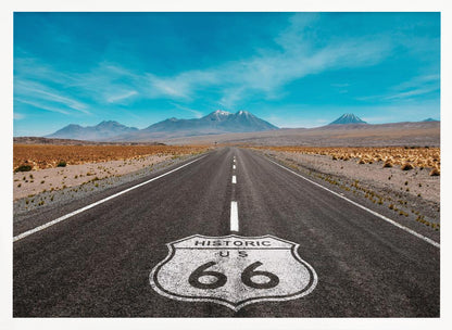 A framed photograph of the iconic Historic US Route 66 shield painted on a long, straight asphalt road that stretches through a desert landscape toward distant snow-capped mountains under a vibrant blue sky. Wall Art