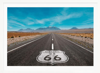 A framed photograph of the iconic Historic US Route 66 shield painted on a long, straight asphalt road that stretches through a desert landscape toward distant snow-capped mountains under a vibrant blue sky. Wall Art
